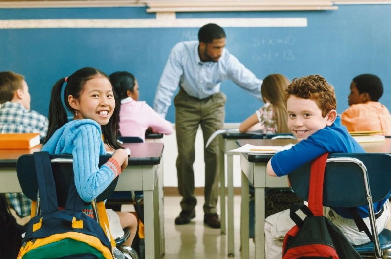 A group of children sitting at desks in front of an adult.